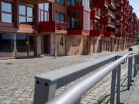 a building with red siding and some balconies in the front of it and a metal bench sitting on the sidewalk outside