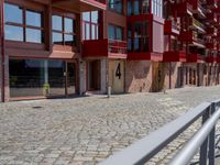 a building with red siding and some balconies in the front of it and a metal bench sitting on the sidewalk outside