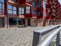 a building with red siding and some balconies in the front of it and a metal bench sitting on the sidewalk outside