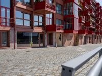 a building with red siding and some balconies in the front of it and a metal bench sitting on the sidewalk outside