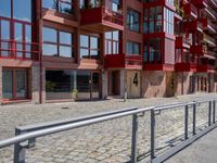 a building with red siding and some balconies in the front of it and a metal bench sitting on the sidewalk outside