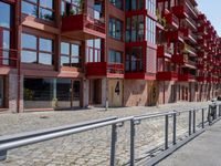 a building with red siding and some balconies in the front of it and a metal bench sitting on the sidewalk outside