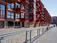 a building with red siding and some balconies in the front of it and a metal bench sitting on the sidewalk outside