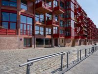 a building with red siding and some balconies in the front of it and a metal bench sitting on the sidewalk outside