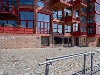 a building with red siding and some balconies in the front of it and a metal bench sitting on the sidewalk outside