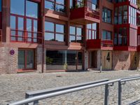 a building with red siding and some balconies in the front of it and a metal bench sitting on the sidewalk outside