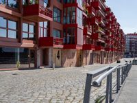 a building with red siding and some balconies in the front of it and a metal bench sitting on the sidewalk outside