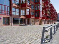 a building with red siding and some balconies in the front of it and a metal bench sitting on the sidewalk outside