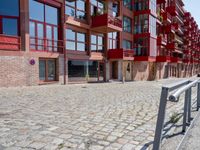 a building with red siding and some balconies in the front of it and a metal bench sitting on the sidewalk outside