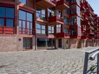 a building with red siding and some balconies in the front of it and a metal bench sitting on the sidewalk outside