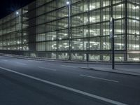 the large building has glass and lights on it's sides on the sidewalk beside a paved roadway