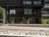 a sidewalk outside of a tall building with a glass front entrance and a bike path