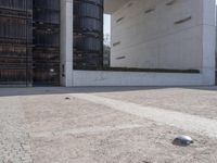 a piece of metal on the ground in front of a building with windows and concrete pillars