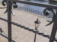 black metal fence near waterway with trees and water in background in public area by waterfront