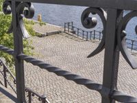 black metal fence near waterway with trees and water in background in public area by waterfront