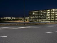 an empty highway by a large building at night time in the dark hour of day