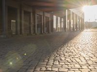 the sun shines behind a row of buildings along a street that has a brick sidewalk and two buildings along side it