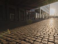 the sun shines behind a row of buildings along a street that has a brick sidewalk and two buildings along side it