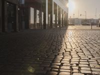 the sun shines behind a row of buildings along a street that has a brick sidewalk and two buildings along side it