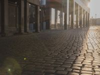 the sun shines behind a row of buildings along a street that has a brick sidewalk and two buildings along side it