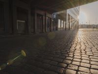 the sun shines behind a row of buildings along a street that has a brick sidewalk and two buildings along side it