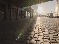the sun shines behind a row of buildings along a street that has a brick sidewalk and two buildings along side it