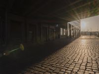 the sun shines behind a row of buildings along a street that has a brick sidewalk and two buildings along side it
