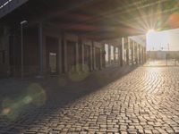 the sun shines behind a row of buildings along a street that has a brick sidewalk and two buildings along side it