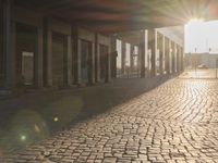 the sun shines behind a row of buildings along a street that has a brick sidewalk and two buildings along side it