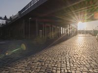 the sun shines behind a row of buildings along a street that has a brick sidewalk and two buildings along side it