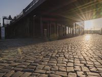 the sun shines behind a row of buildings along a street that has a brick sidewalk and two buildings along side it