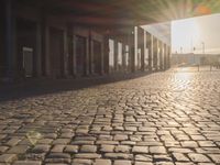the sun shines behind a row of buildings along a street that has a brick sidewalk and two buildings along side it