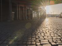 the sun shines behind a row of buildings along a street that has a brick sidewalk and two buildings along side it