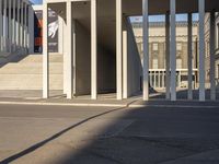 the large, empty sidewalk with multiple columns in front of the building with two signs