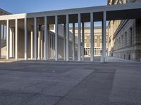 the large, empty sidewalk with multiple columns in front of the building with two signs