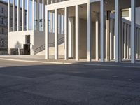 the large, empty sidewalk with multiple columns in front of the building with two signs