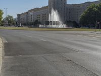 the building is very large and tall by the water fountain in the middle of the street