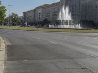 the building is very large and tall by the water fountain in the middle of the street