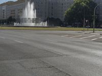 the building is very large and tall by the water fountain in the middle of the street