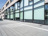 a building with glass windows on top of it and sidewalk in front of it and people walking beside it