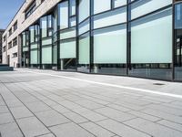 a building with glass windows on top of it and sidewalk in front of it and people walking beside it