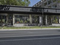 a store with no cars on the street next to a tree and grass field near a street