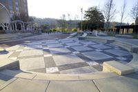 circular park with lots of gray tiles and white pillars surrounding it with benches in front of the building