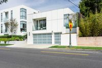 white house with garage and attached elevator on an empty street with trees around it and one yellow car in front