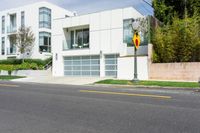 white house with garage and attached elevator on an empty street with trees around it and one yellow car in front