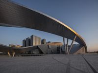 the large modern building has a curved structure over it's roof area to the right