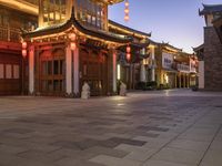 the illuminated entrance to an asian styled building at night with lanterns on it's sides