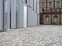 two people are walking down a cobble stone street while two buildings have closed them