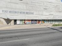 a car driving down the street in front of a museum building with billboards on the side