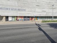 a car driving down the street in front of a museum building with billboards on the side